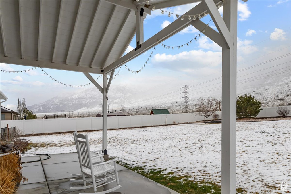 Snow covered patio featuring a mountain view and a fenced backyard
