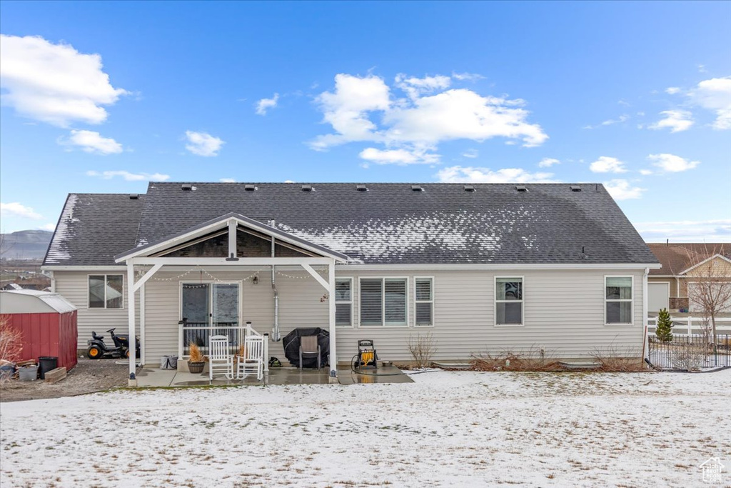 Snow covered rear of property featuring a patio and roof with shingles