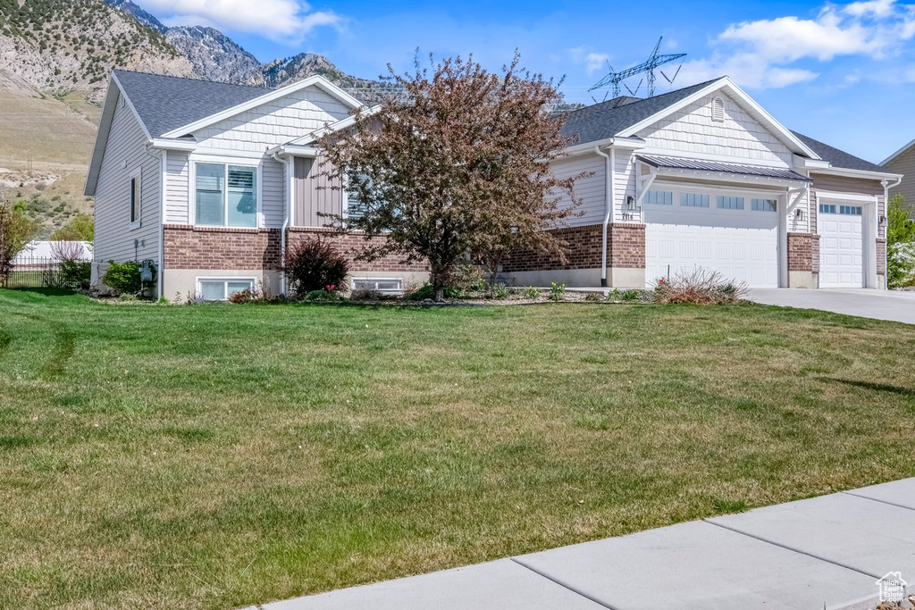View of front facade featuring concrete driveway, an attached garage, a mountain view, a front yard, and brick siding