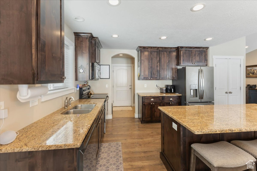 Kitchen featuring dark brown cabinetry, arched walkways, appliances with stainless steel finishes, and a sink