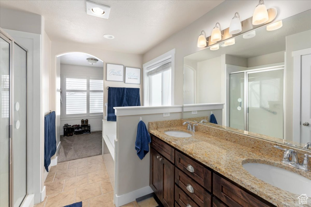 Full bath with double vanity, baseboards, a stall shower, and a sink