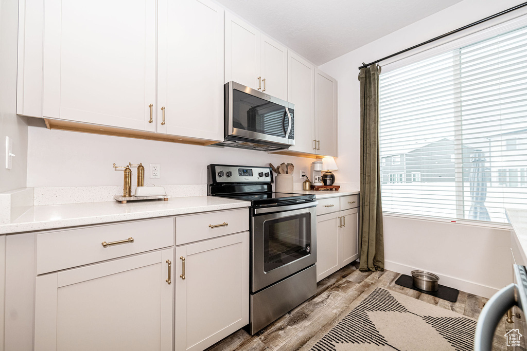 Kitchen featuring white cabinets, appliances with stainless steel finishes, light wood-type flooring, and light countertops