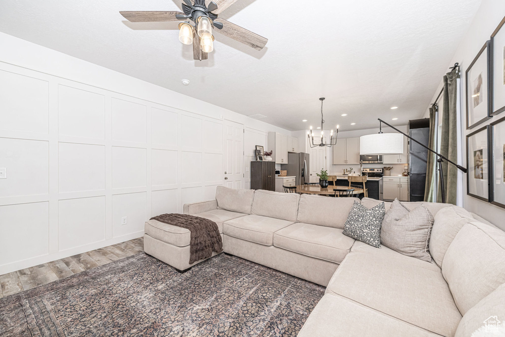 Living area with recessed lighting, light wood-type flooring, ceiling fan with notable chandelier, and a decorative wall
