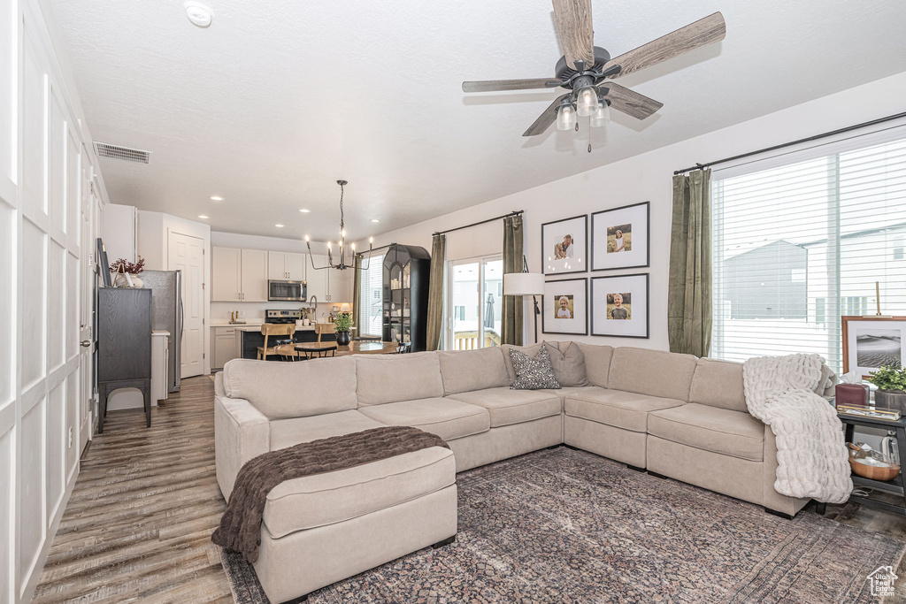 Living room with recessed lighting, ceiling fan with notable chandelier, visible vents, and light wood finished floors