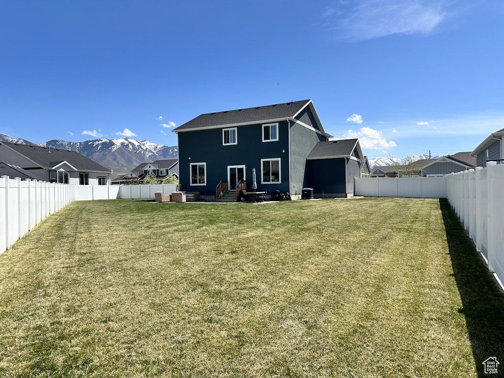 Back of house with a fenced backyard, a mountain view, a yard, a patio, and an outdoor living space