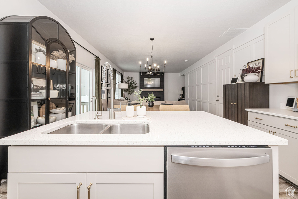 Kitchen featuring a sink, stainless steel dishwasher, open floor plan, light stone countertops, and a chandelier