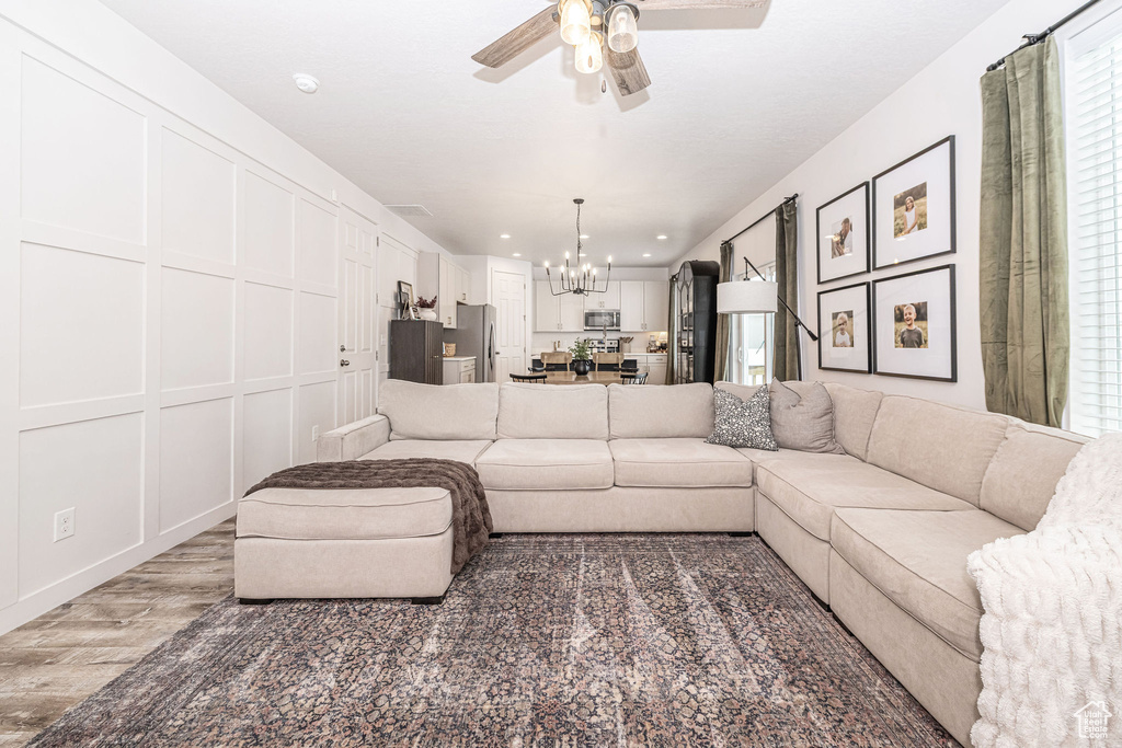 Living room featuring a decorative wall, recessed lighting, ceiling fan with notable chandelier, and light wood-style flooring