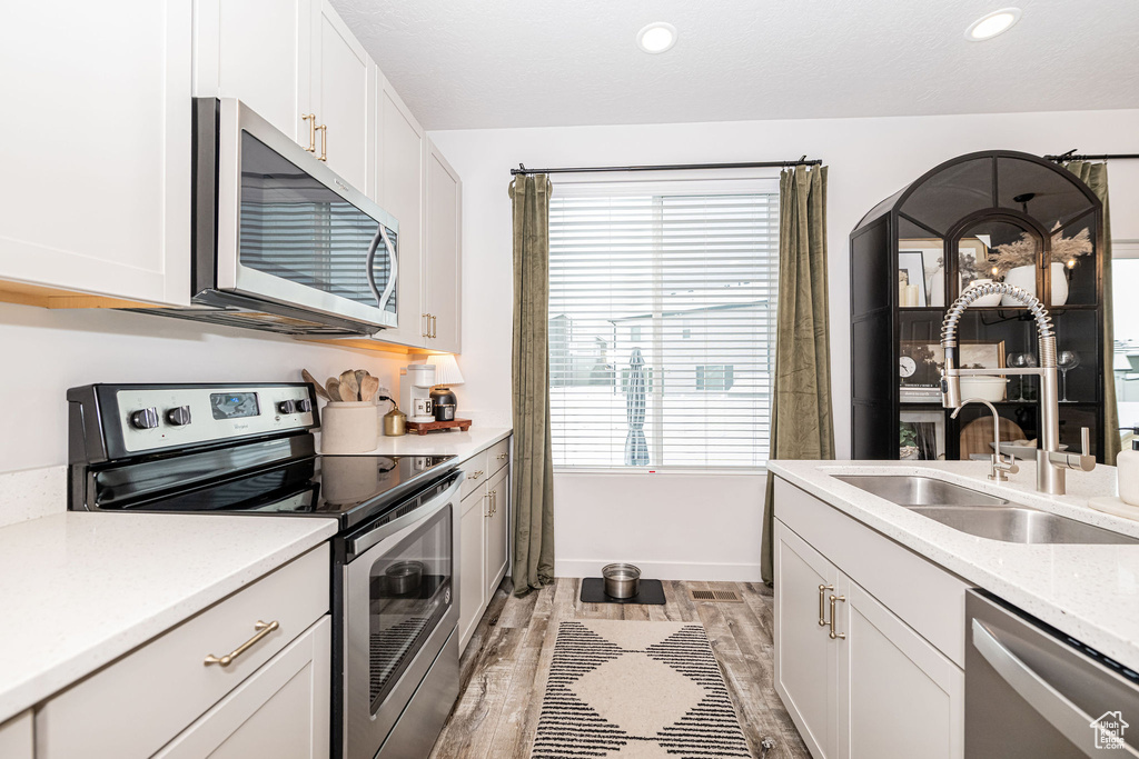 Kitchen featuring light wood-type flooring, light countertops, stainless steel appliances, white cabinetry, and a sink