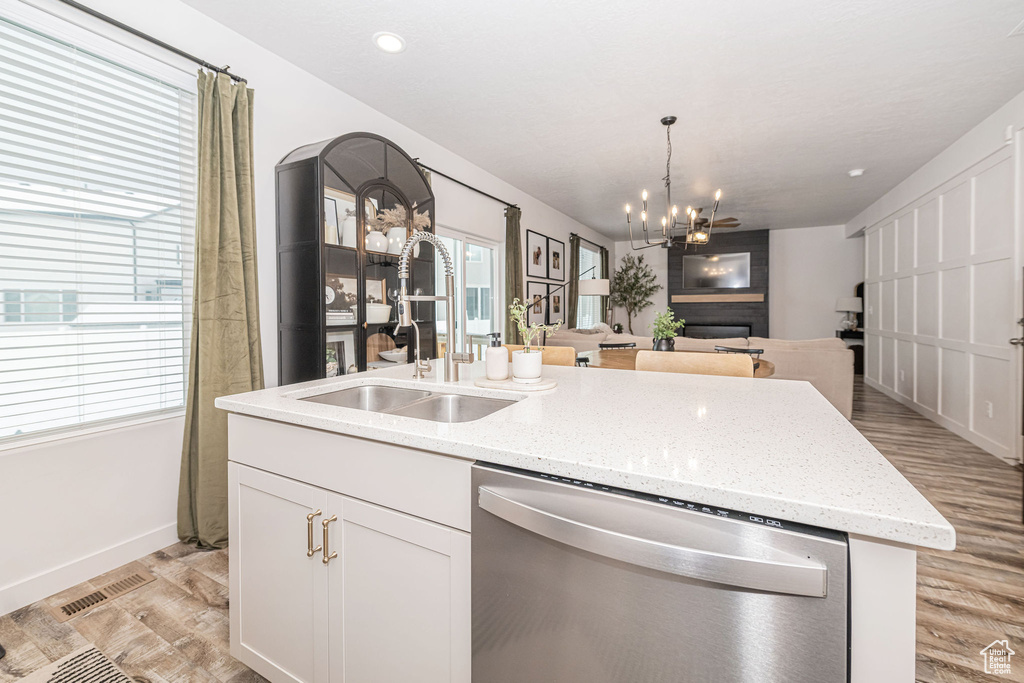 Kitchen with a center island with sink, a sink, dishwasher, open floor plan, and a chandelier