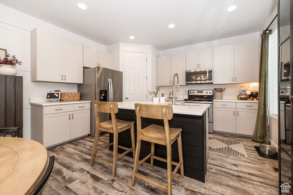 Kitchen featuring a sink, light countertops, light wood-style floors, stainless steel appliances, and a kitchen island with sink