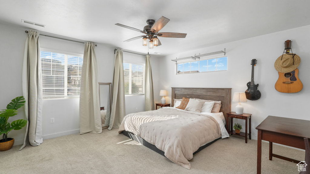 Carpeted bedroom featuring visible vents, multiple windows, baseboards, and ceiling fan