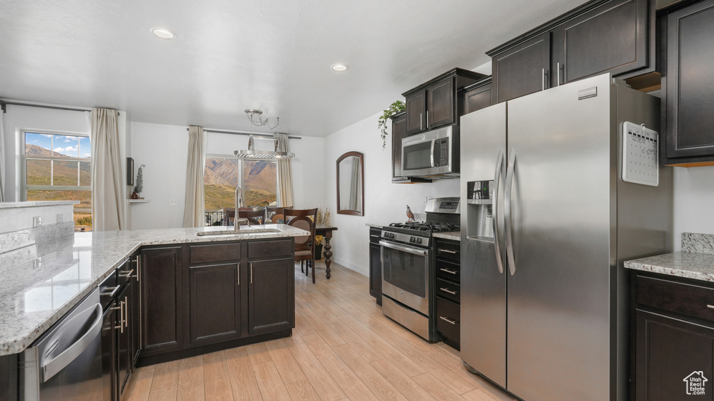 Kitchen with baseboards, light wood-type flooring, light stone counters, stainless steel appliances, and a sink