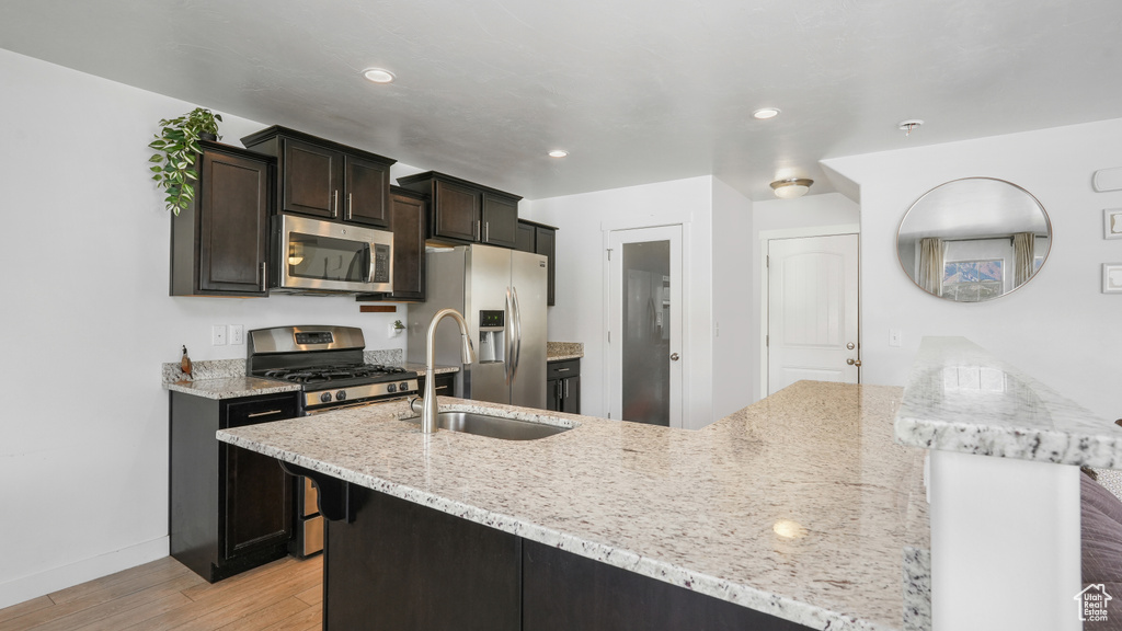 Kitchen with light stone countertops, baseboards, light wood finished floors, a sink, and stainless steel appliances