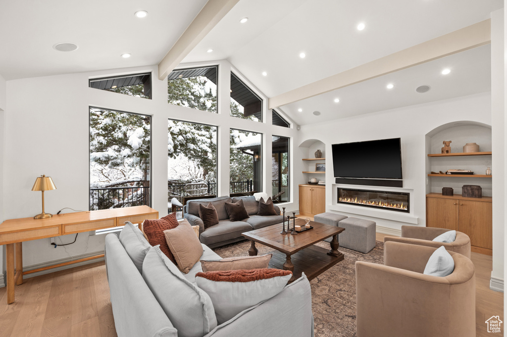 Living area with a glass covered fireplace, beamed ceiling, built in shelves, and light wood-type flooring