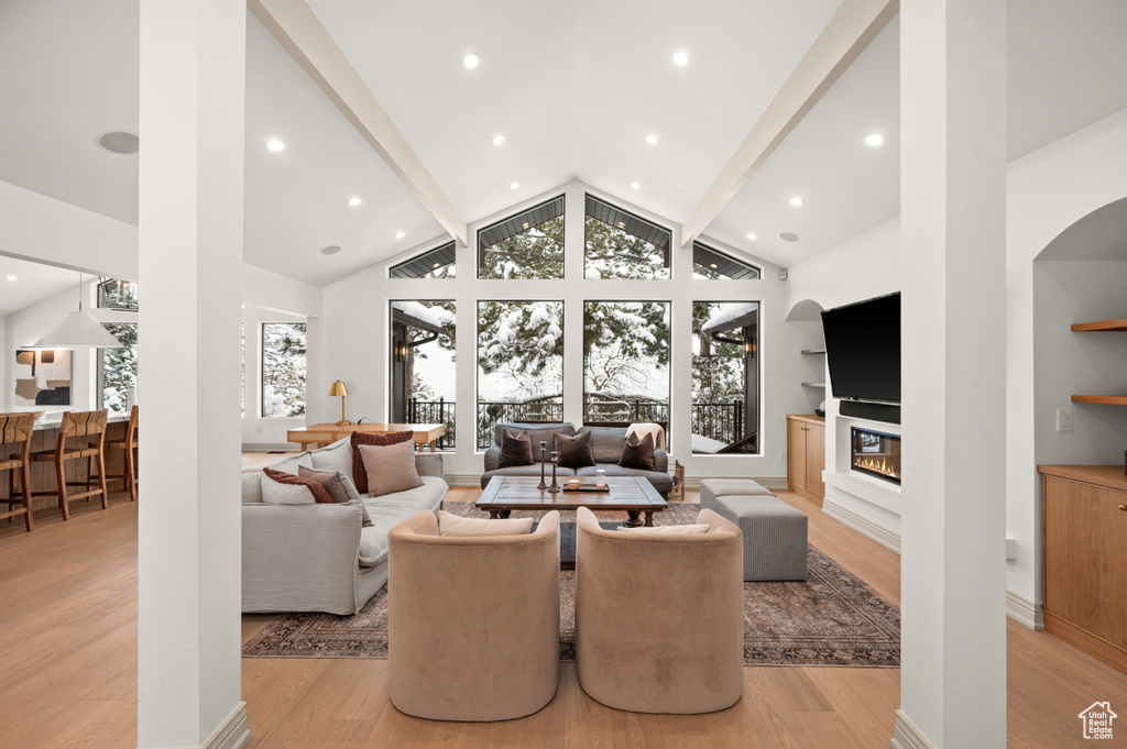 Living area with a glass covered fireplace, a healthy amount of sunlight, light wood finished floors, and high vaulted ceiling