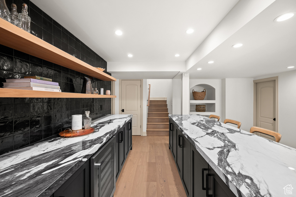 Kitchen featuring open shelves, light stone counters, and dark cabinets