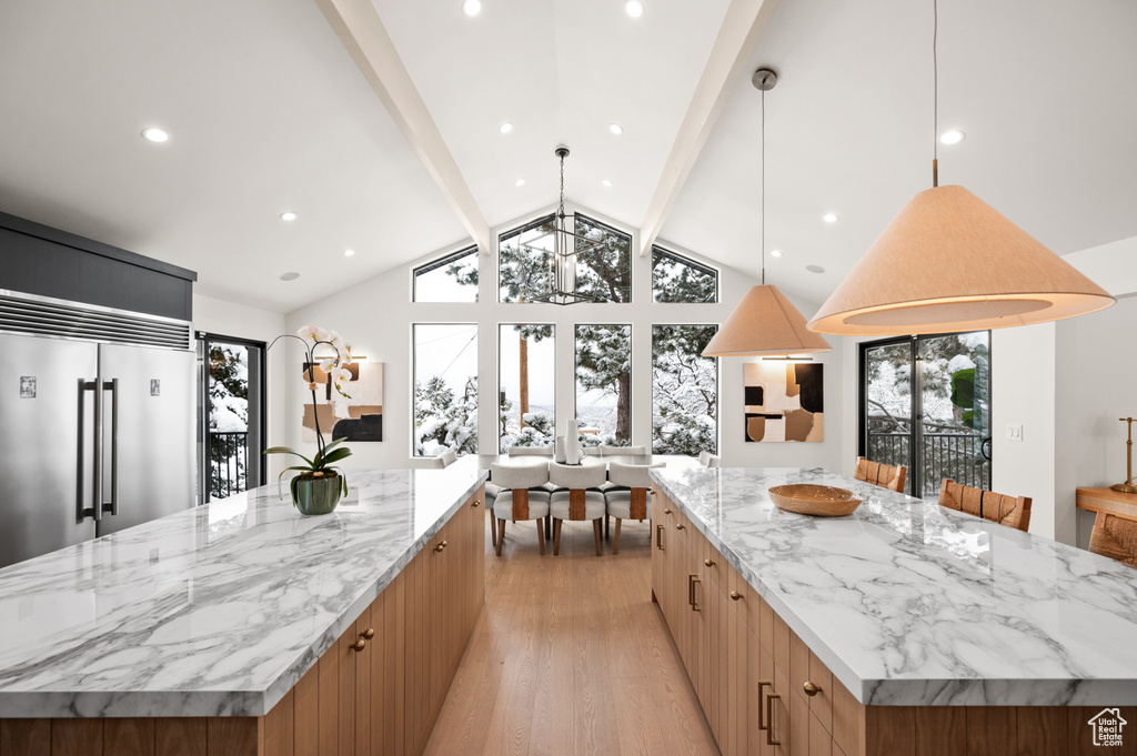 Kitchen with light stone countertops, a large island, built in fridge, modern cabinets, and light wood-type flooring