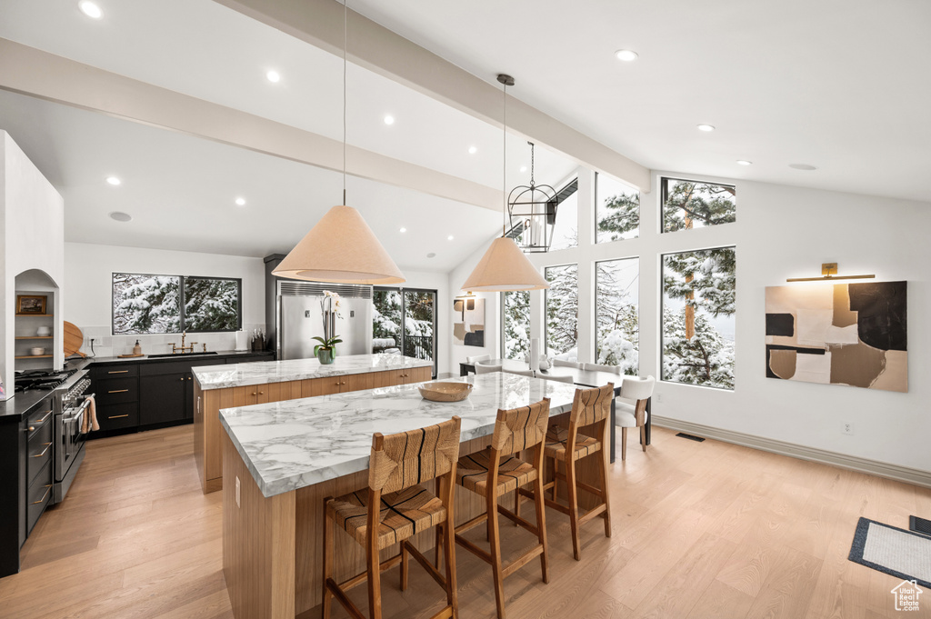 Kitchen featuring a spacious island, vaulted ceiling with beams, premium appliances, light wood-style flooring, and dark cabinets