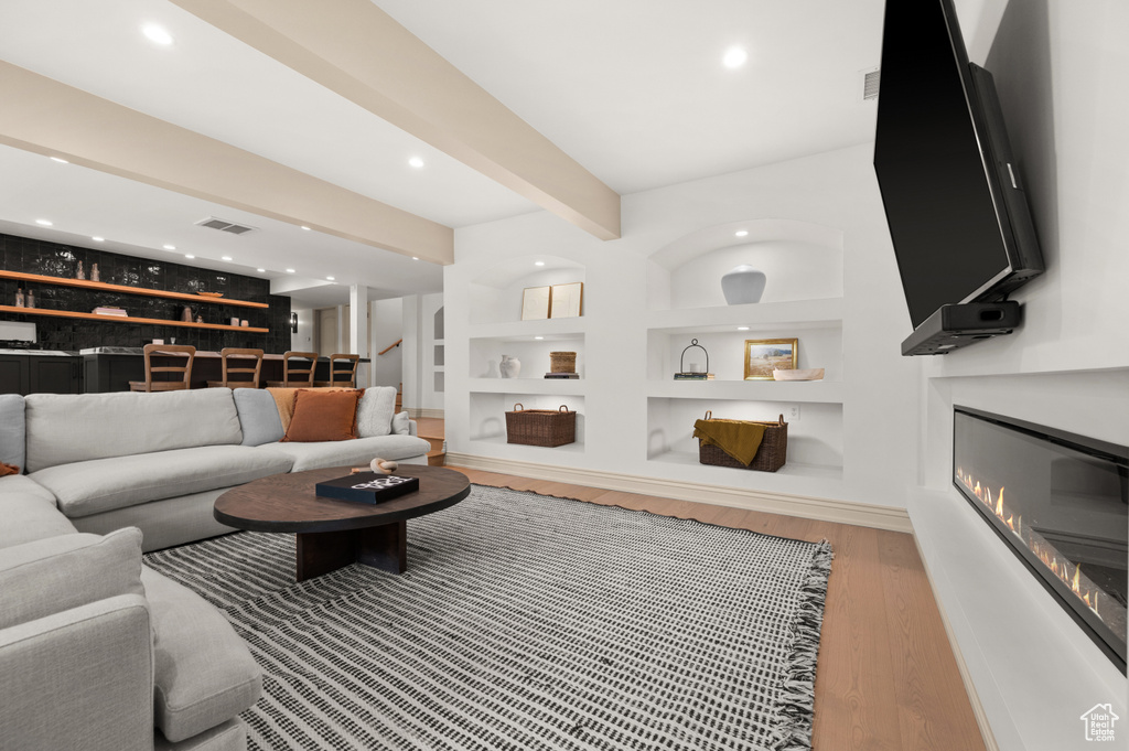 Living room with stairway, wood finished floors, visible vents, a glass covered fireplace, and beamed ceiling