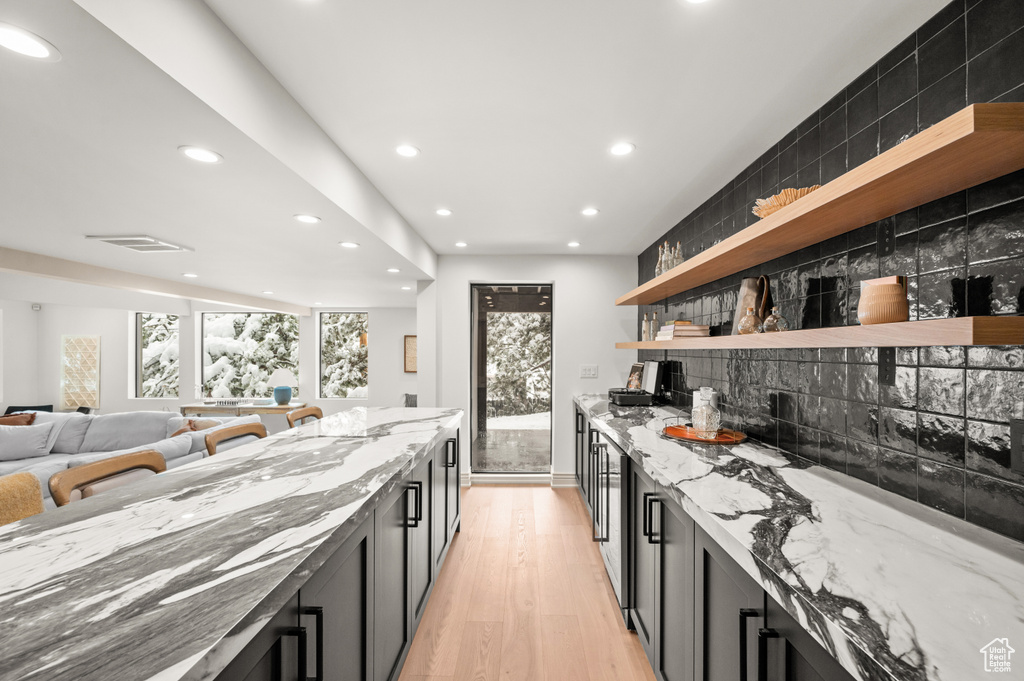 Kitchen with backsplash, open shelves, dark cabinetry, and light stone countertops