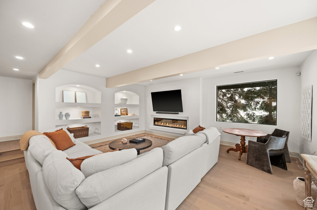 Living area featuring a glass covered fireplace, beam ceiling, recessed lighting, and light wood-type flooring