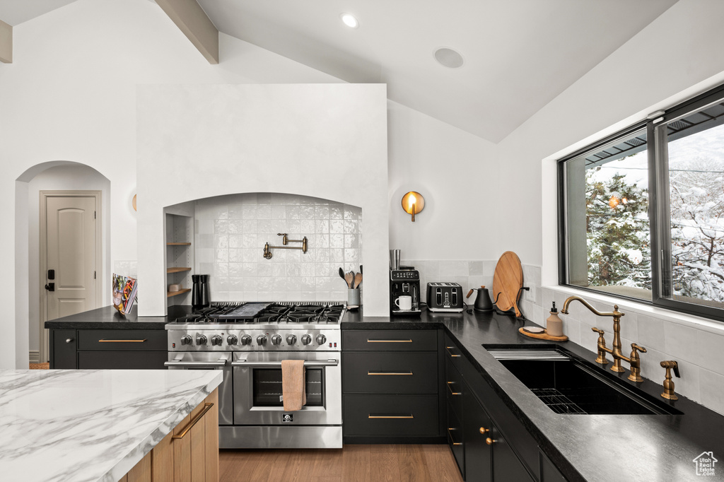 Kitchen with light wood-style flooring, double oven range, lofted ceiling, and a sink