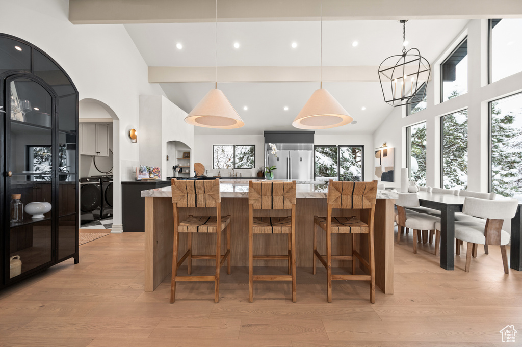 Interior space featuring a spacious island, washing machine and clothes dryer, arched walkways, light wood-style floors, and beamed ceiling