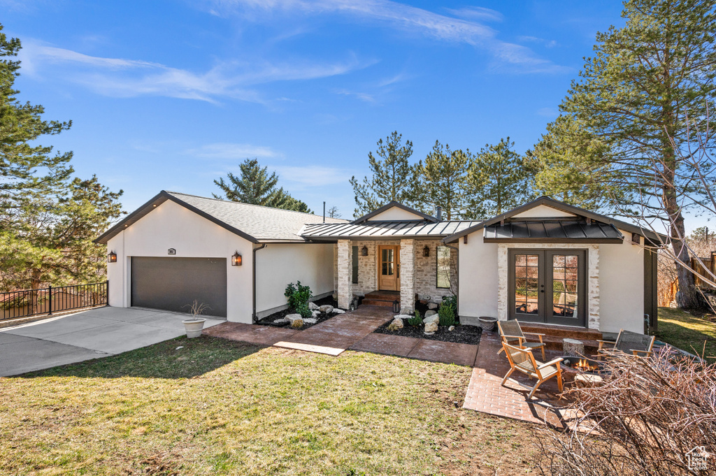 View of front of house featuring a front lawn, driveway, a standing seam roof, french doors, and a garage