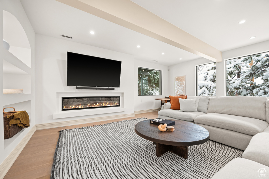 Living area with visible vents, beam ceiling, recessed lighting, light wood-style floors, and a glass covered fireplace