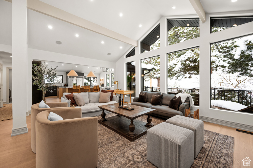 Living room with light wood finished floors, visible vents, beamed ceiling, and high vaulted ceiling