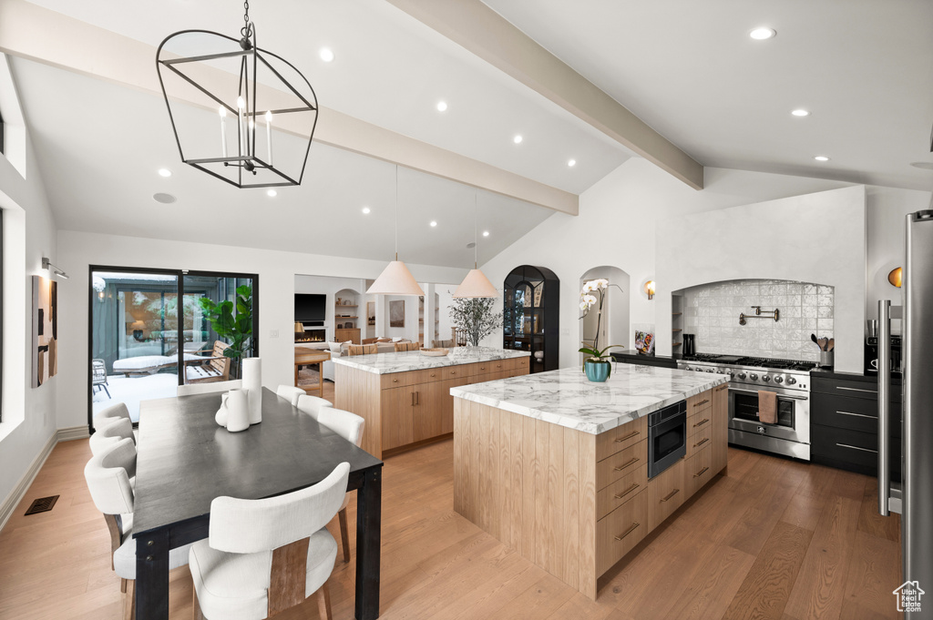 Kitchen featuring lofted ceiling with beams, arched walkways, a large island, appliances with stainless steel finishes, and modern cabinets