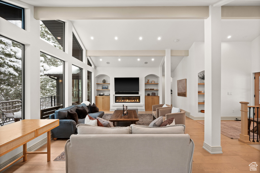 Living area with light wood finished floors, baseboards, built in features, a glass covered fireplace, and high vaulted ceiling