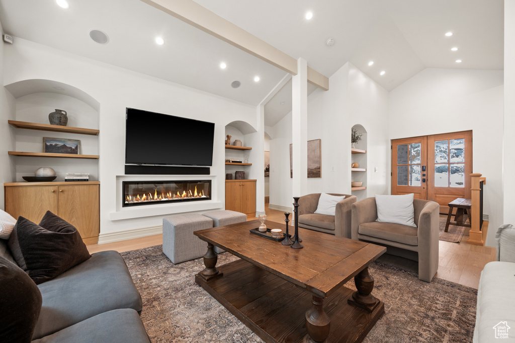 Living area featuring built in shelves, high vaulted ceiling, light wood-style flooring, recessed lighting, and a glass covered fireplace