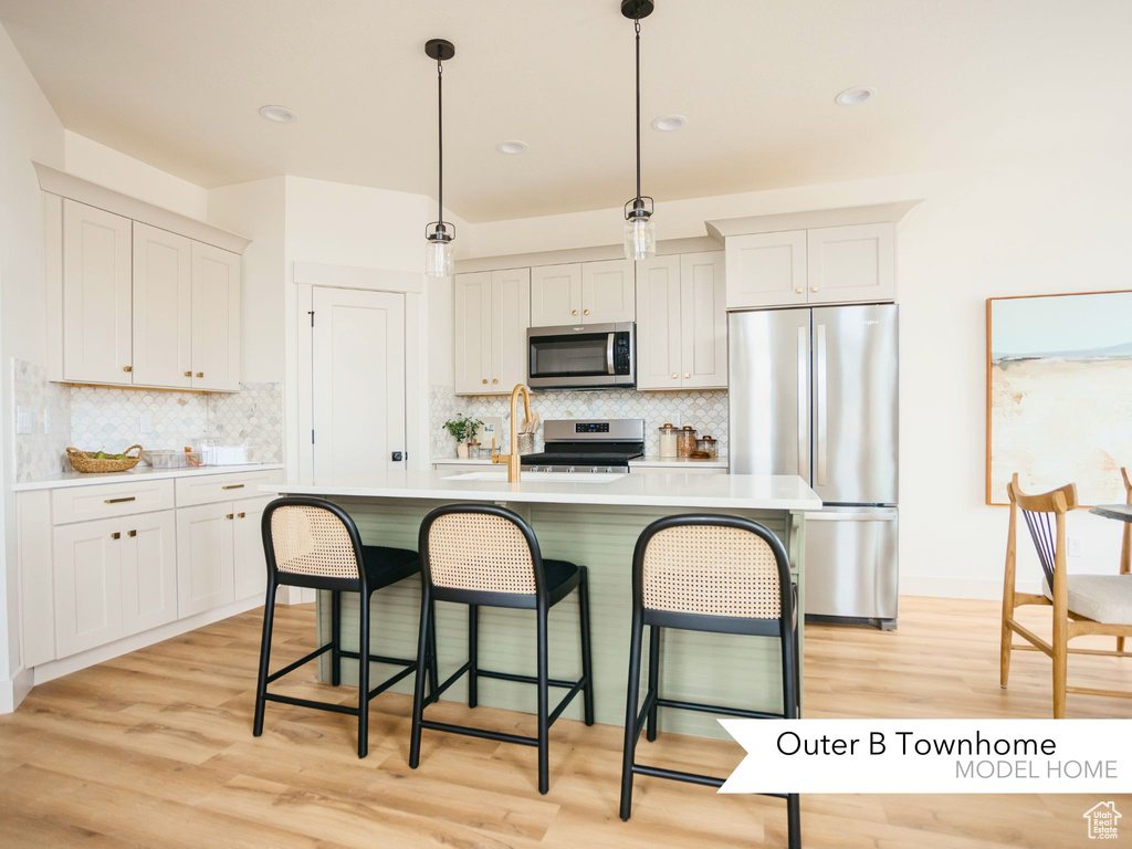 Kitchen with light wood-type flooring, a breakfast bar, decorative light fixtures, appliances with stainless steel finishes, and light countertops