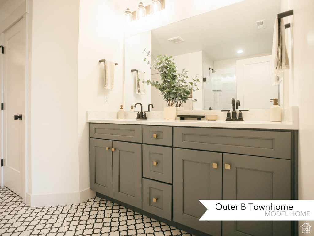 Full bathroom featuring double vanity, visible vents, a stall shower, and baseboards
