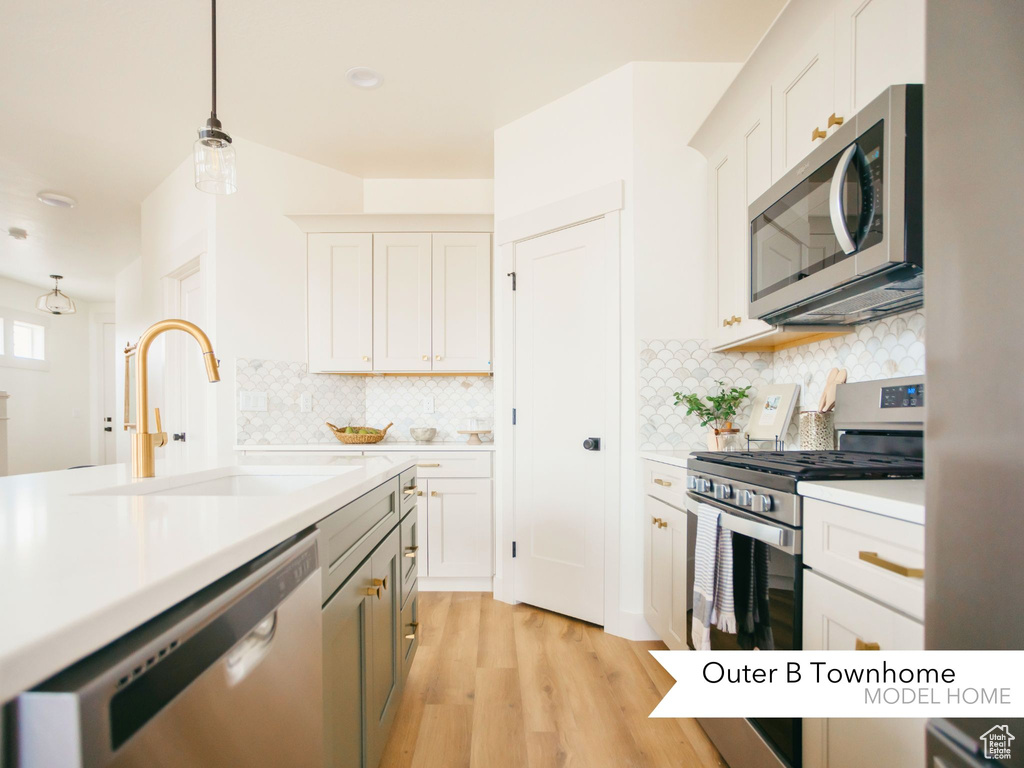 Kitchen with decorative light fixtures, light countertops, decorative backsplash, appliances with stainless steel finishes, and a sink