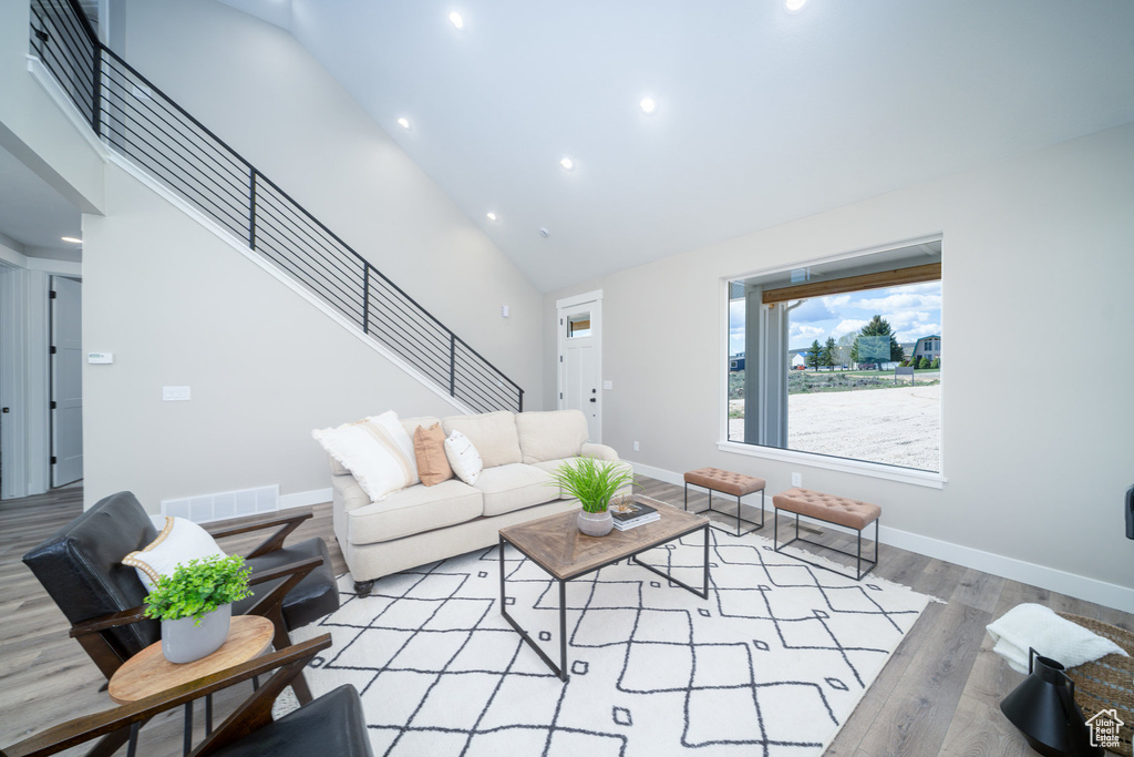 Living room with stairs, wood finished floors, high vaulted ceiling, visible vents, and recessed lighting