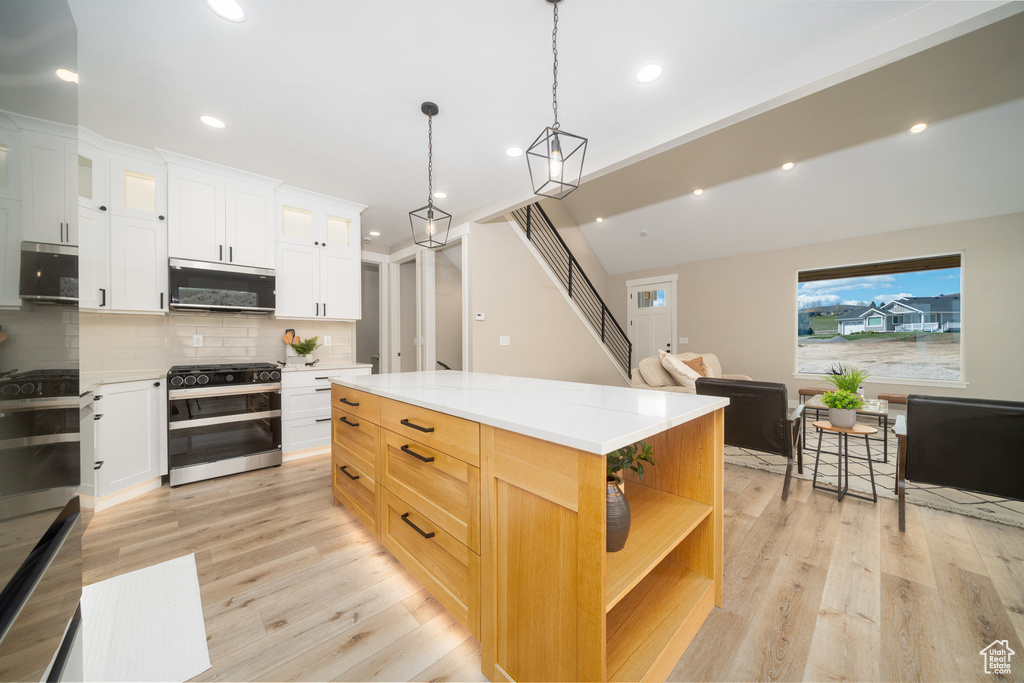 Kitchen featuring stainless steel microwave, light wood-style flooring, tasteful backsplash, and range with two ovens