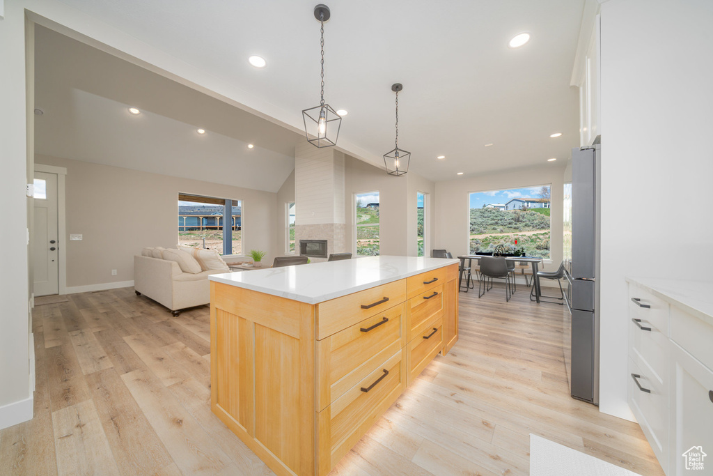 Kitchen with light brown cabinets, open floor plan, a multi sided fireplace, and light wood-style flooring