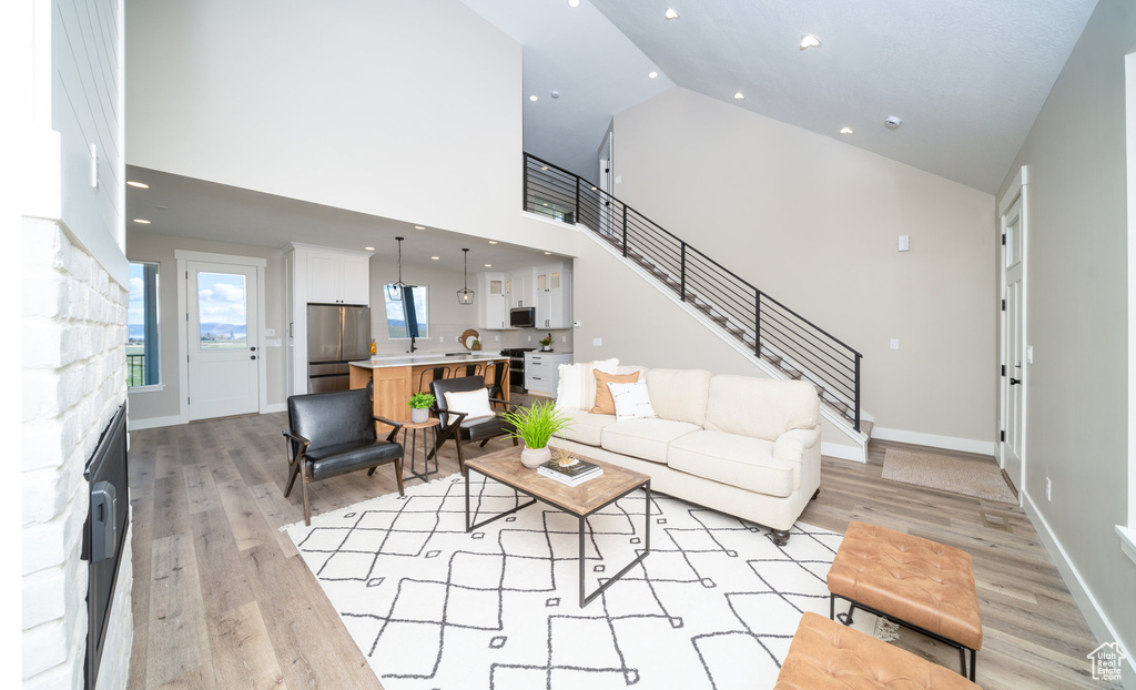 Living room with high vaulted ceiling, light wood-type flooring, a stone fireplace, and stairway