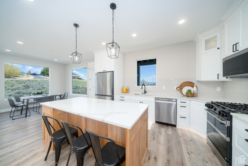 Kitchen with light wood finished floors, a healthy amount of sunlight, appliances with stainless steel finishes, and a kitchen bar