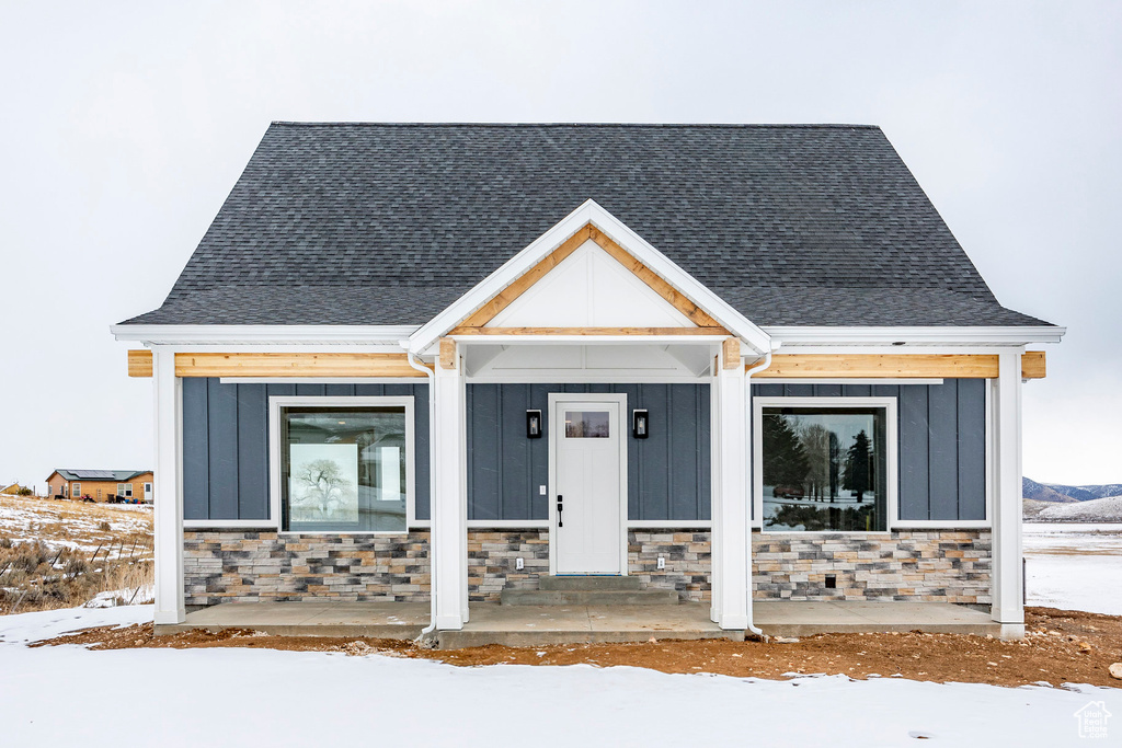 View of front of property featuring roof with shingles, stone siding, and board and batten siding