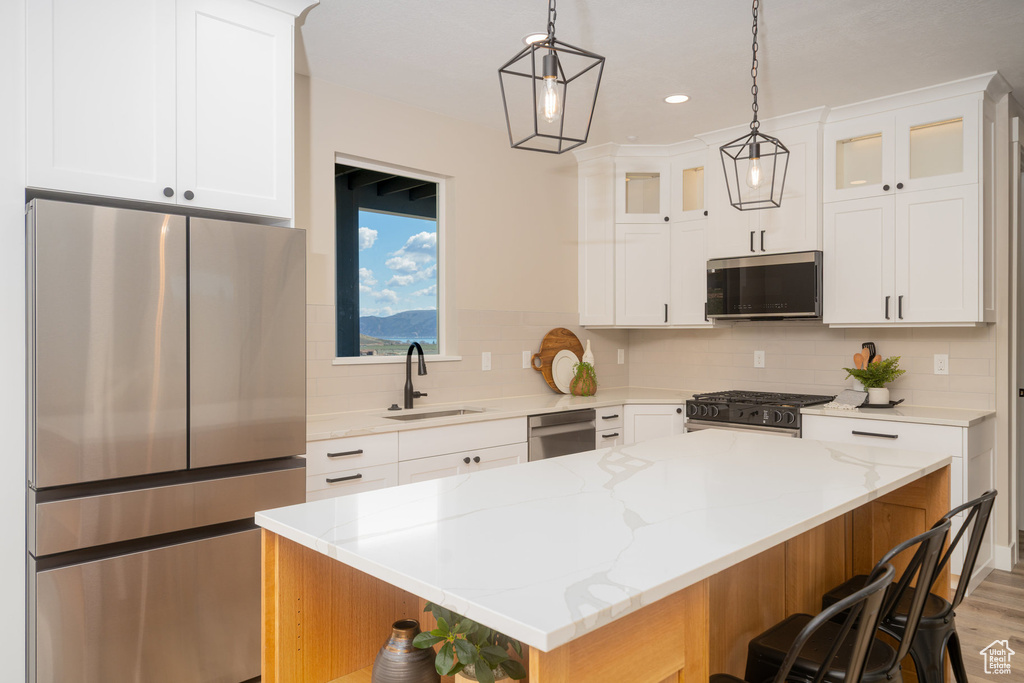 Kitchen with a sink, stainless steel appliances, tasteful backsplash, a breakfast bar, and glass insert cabinets