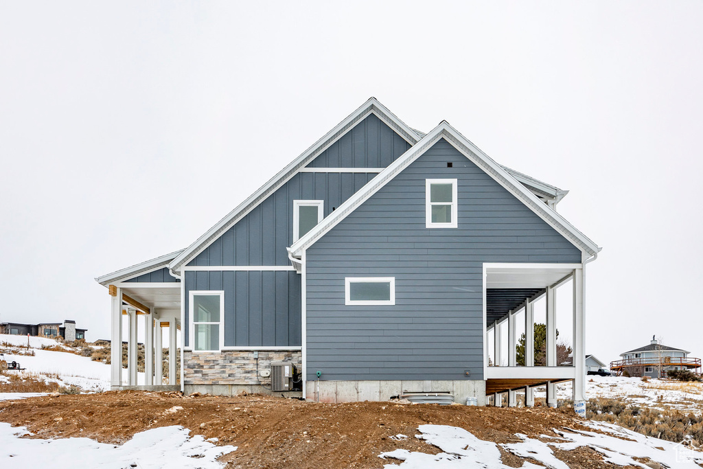 View of snowy exterior featuring central AC unit, stone siding, and board and batten siding