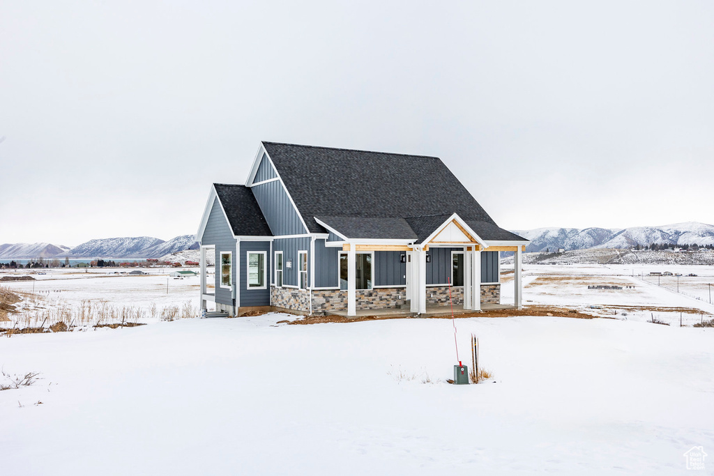 View of front of home with board and batten siding, a mountain view, stone siding, a porch, and roof with shingles