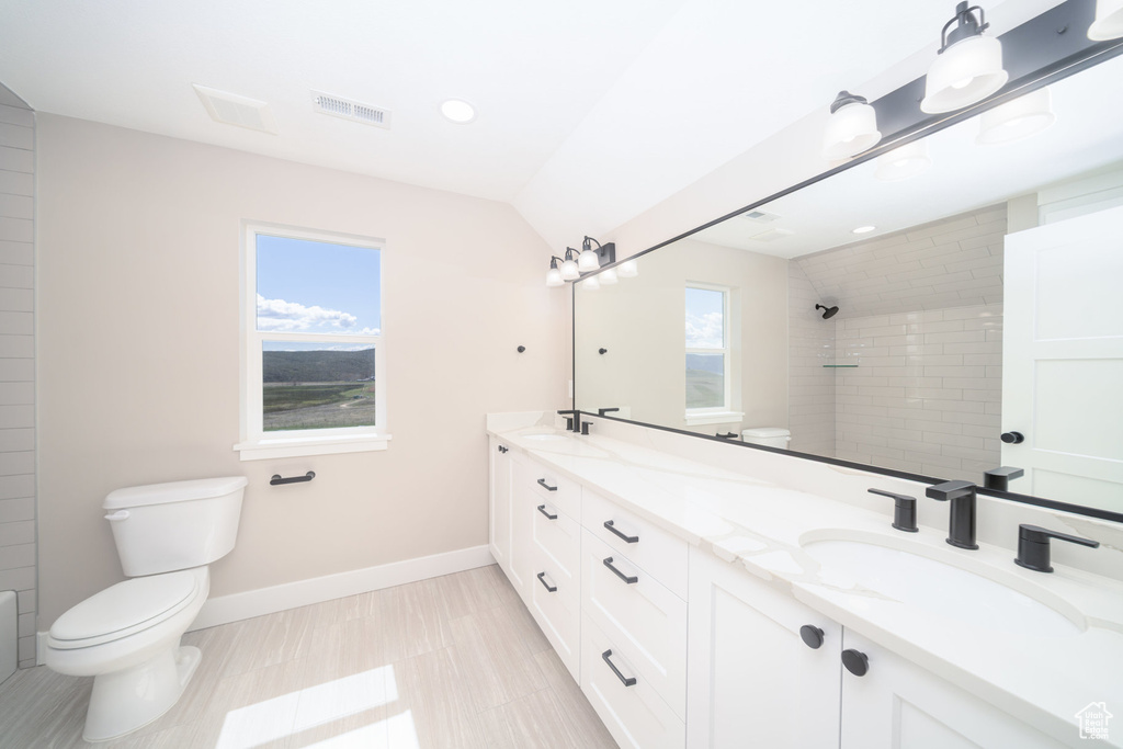 Bathroom featuring toilet, tiled shower, visible vents, and a sink
