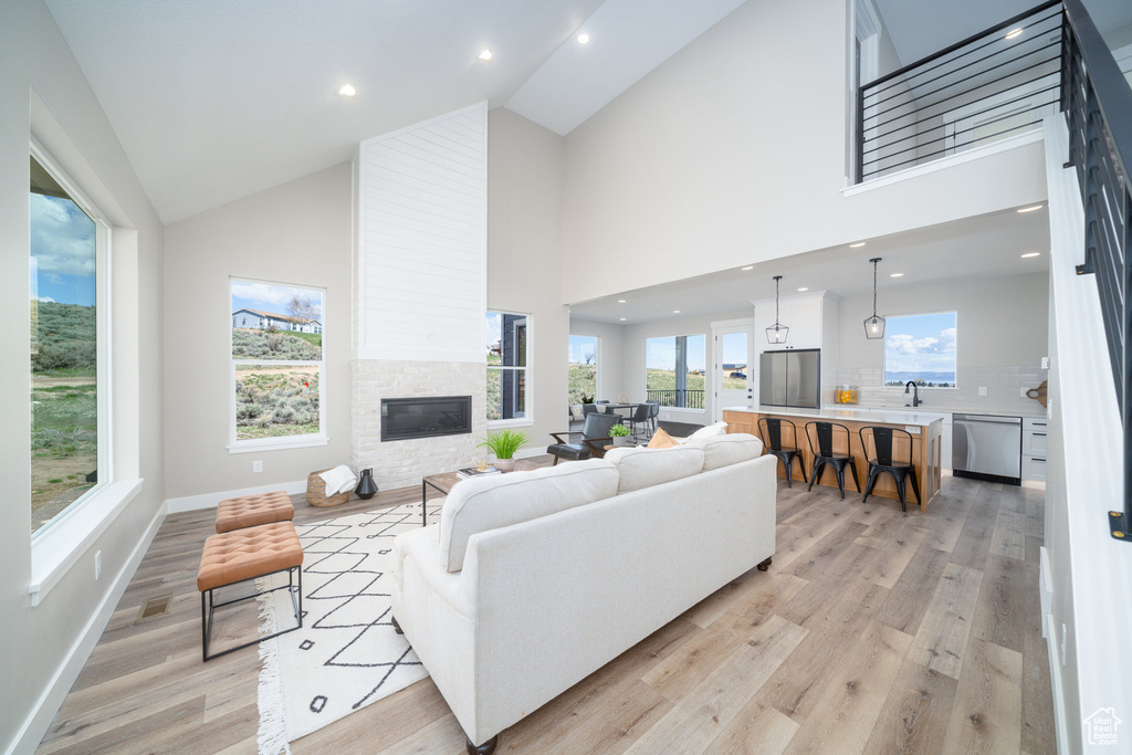 Living room with high vaulted ceiling, a fireplace, baseboards, light wood-style floors, and recessed lighting