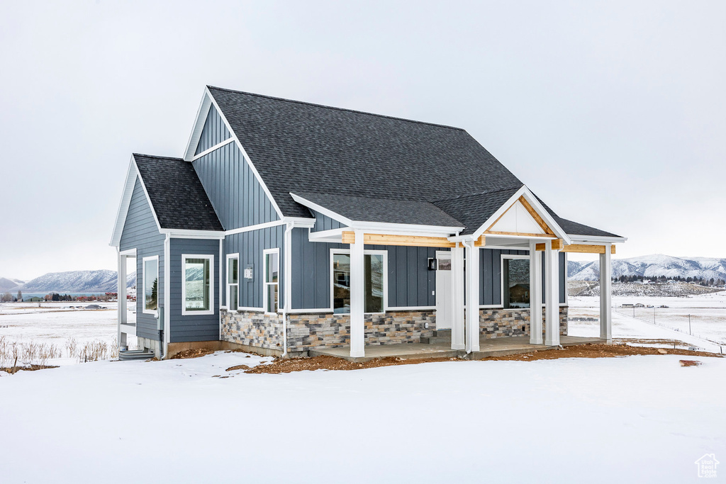 View of front of home featuring board and batten siding, a mountain view, stone siding, a porch, and roof with shingles