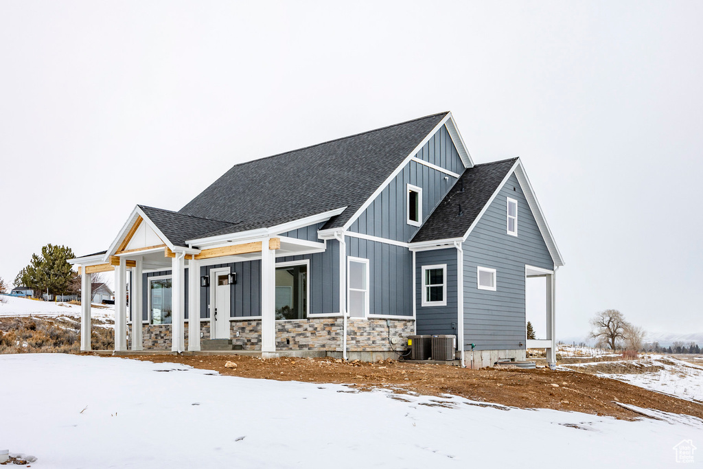 Snow covered property featuring board and batten siding, roof with shingles, covered porch, and stone siding