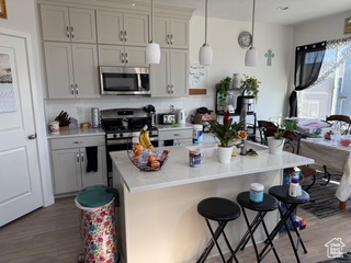 Kitchen featuring a breakfast bar area, wood finished floors, stainless steel appliances, light countertops, and pendant lighting